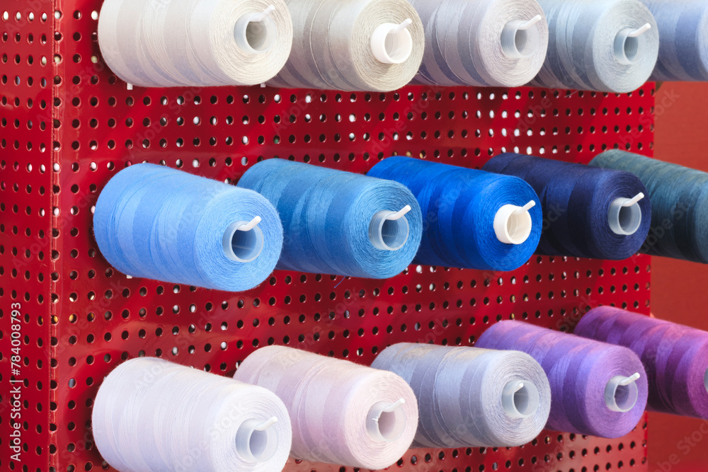 Leinwandbilder a rack of colorful spools of thread is hanging on a red wall. the spools are of various colors and s
