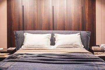 A bed with two pillows and a blue blanket. The bed is in a room with wooden walls and a wooden headboard