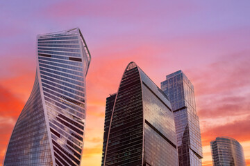 Obraz premium A city skyline with a beautiful sunset in the background. The buildings are tall and shiny, and the sky is a mix of orange and pink hues. Concept of awe and wonder at the beauty of the cityscape