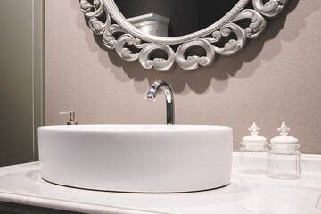 A white sink with a silver faucet sits in front of a mirror. The mirror is ornate and adds a touch...