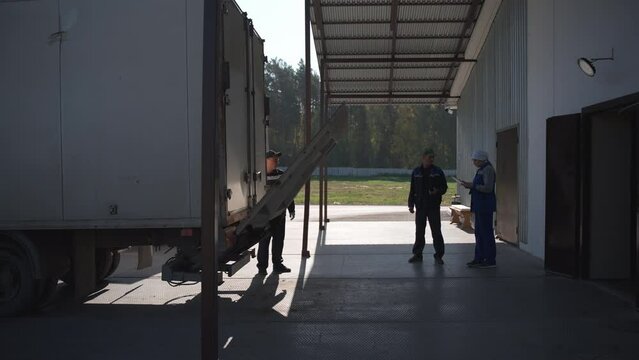 Lowering the automated truck ramp to offload the cargo delivery to the warehouse. Transferring the cargo delivery products to the factory warehouse. Warehouse workers deal with the cargo delivery.