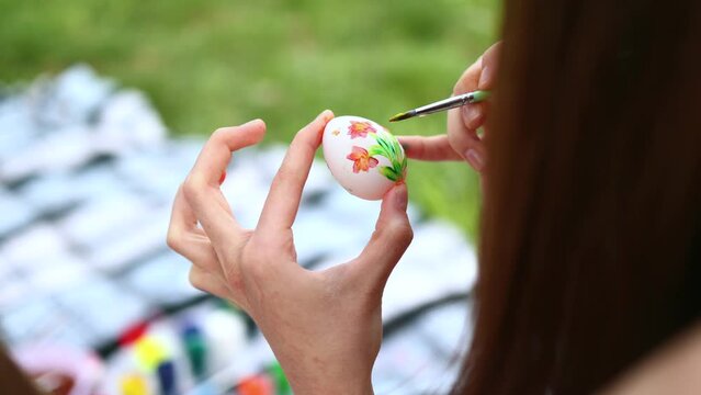 Girls' hands paint Easter eggs with paints of different colors in the open air. Watercolor painting on eggs. Close-up video of hands