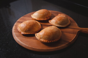 Freshly baked empanadas on top of a round wooden tray.