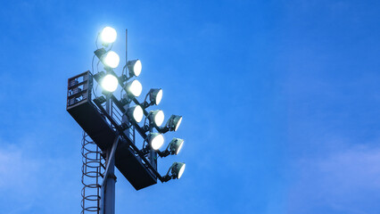 A floodlight tower illuminated, standing tall against the evening blue sky background with copy space. - obrazy, fototapety, plakaty