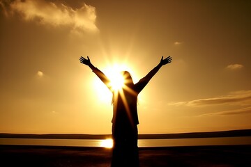 Fototapeta premium Silhouette of a woman standing at sunset, with raised arms in worship and praise, symbolizing