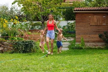 Mother with kids run through sprinkling water in verdant garden - 784030983
