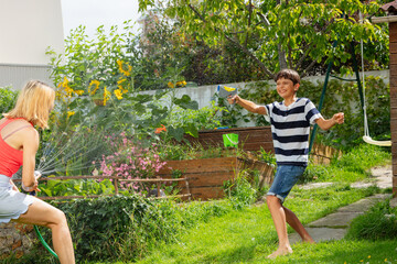 Teen laughs while engage in a water gun game with his mother - 784031324
