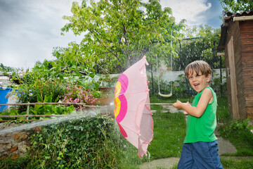 Boys enjoy water fight in garden hiding behind pink umbrella - 784032102