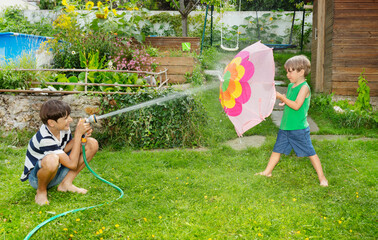 Boys enjoy water fight in garden one shelters behind umbrella - 784033757