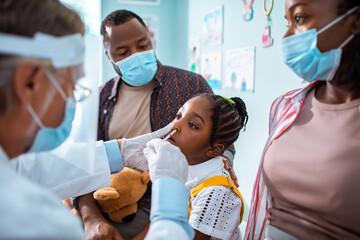 Child receiving nasal vaccine at pediatrician's office with parents present
