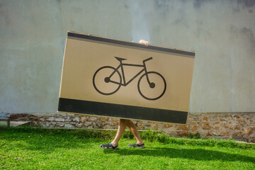 Person hide and carrying an enormous box marked with a bike logo - 784037739