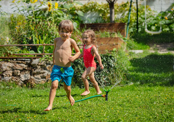 Playful boy and girl enjoying a sprinkle of water run around - 784038737