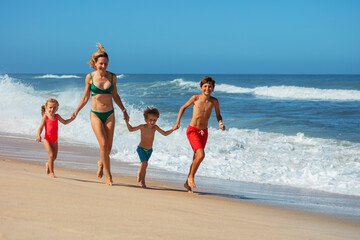 Joyful beach run with kids and their mom in colorful swimsuits - 784041716