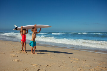 Kids walking with surfboard on shoulders at sunny ocean beach - 784043922