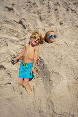 Two kids buried in sand, smiling with shades, view from above - 784045129