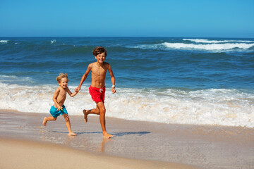 Two young boys joyfully run along the sandy ocean beach resort - 784046974