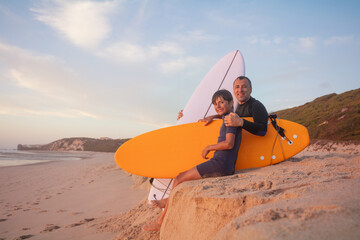 Father and son enjoying beach day with a surfboard at sunset - 784049740