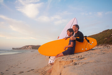 Man and young boy with surfboards at the seashore during dusk - 784050361