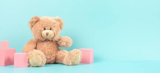 Baby kids toys banner background. Small teddy bear and pink wooden cubes on pastel blue background. Front view