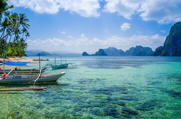 Banca boats in clear water at sandy beach in El Nido, Philippines