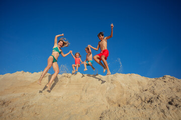 Happy family with kids and mother having fun jumping on sand - 784053588