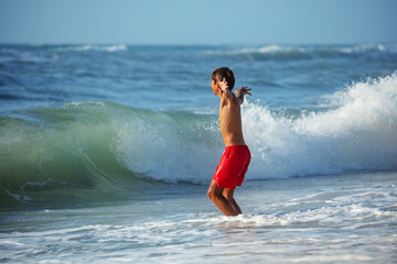 Child in red swim gear enjoys playful embrace of shoreline waves - 784053983
