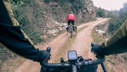 Riding a gravel bike with drop bar on a bikepacking trip over a muddy gravel track rider point of view