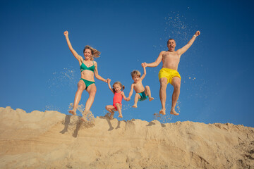 Family enjoys a cheerful sand beach jump holding hands together - 784056119