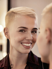 Eine junge blonde Frau betrachtet sich im Spiegel und lächelt. KI generiert. - 784056582