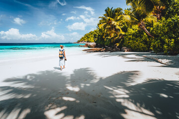 Female tourist enjoy empty tropical beach on vacation. White sand beach, palm trees and blue ocean lagoon. Exotic paradise recreation vacation concept