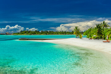Palm trees and beach umbrelllas over lagoon and sandy beach, Maldives island - obrazy, fototapety, plakaty