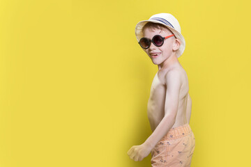 Portrait of a happy boy 6-7 years old in a hat and swimming shorts on a yellow background, sea and summer