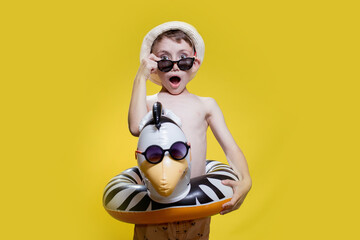 Boy in summer panama and sunglasses with inflatable swimming circle on yellow background