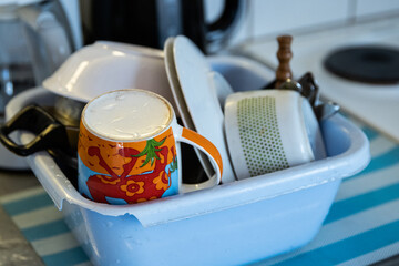 Clean dishes - cups, plates, bowls, cooking pot are getting dry in the broken blue washbowl at the...