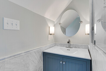 Sleek Contemporary Bathroom Featuring a Blue Cabinet Vanity, Marble Walls, and A Unique Oval Mirror