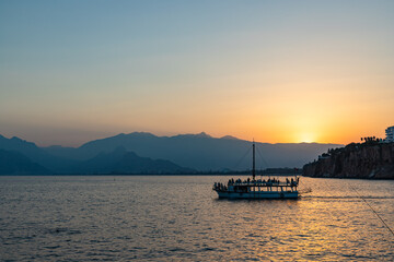 Naklejka premium ANTALYA, TURKYE - SEPTEMBER 17, 2022: Old harbour in Antalya at sunset with tourists boat at front