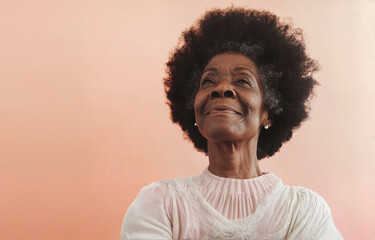 Obraz na płótnie Canvas A beautiful mature African American woman of 70 years smiles and gazes at the horizon against a soft, neutral peach background.