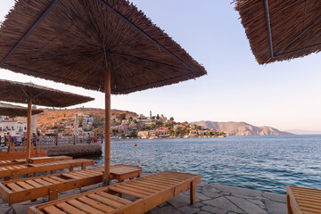 Sun loungers over the sea on the embankment of the village Symi.