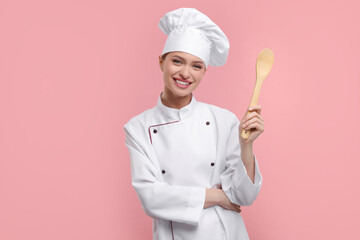 Happy chef in uniform holding wooden spoon on pink background