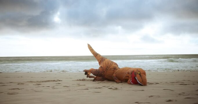 Inflatable dinosaur, beach and happy with jump for entertainment as performer or playful with fun and excited in Florida. Costume, mascot and character at ocean for recreation, relax and enjoy.