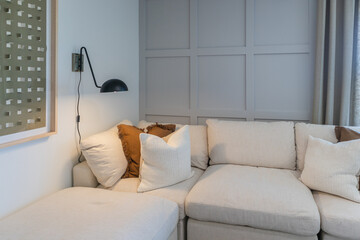 Corner beige sectional sofa with black lamp for reading against gray square paneled wall