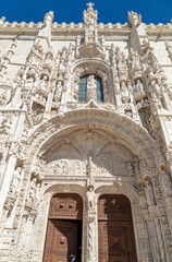 Fototapeta na wymiar Ornate Carved White LimeStone Facade of Mosteiro dos Jeronimos Monastery, Two Wooden Doors Entrance, Lisbon, Portugal