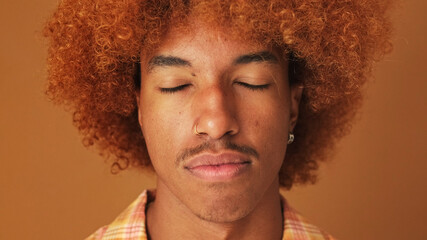 Close up, portrait of a stylish curly guy standing with his eyes closed, isolated on brown...