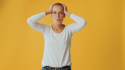 Shocked young hairless woman, looking at camera with big eyes, says wow, isolated on yellow background in studio