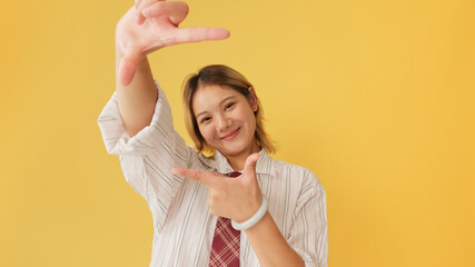 Young woman looking at camera shows compositional gesture, isolated on yellow background