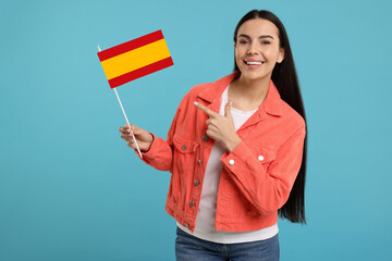 Happy young woman pointing at flag of Spain on light blue background