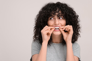 Young woman applying whitening strip on her teeth against light grey background, space for text