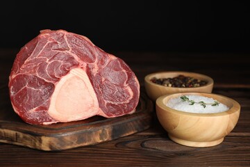 Piece of raw beef meat and spices on wooden table against black background, closeup