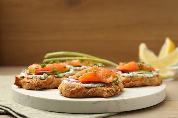 Tasty canapes with salmon, cucumber, radish and cream cheese on wooden table