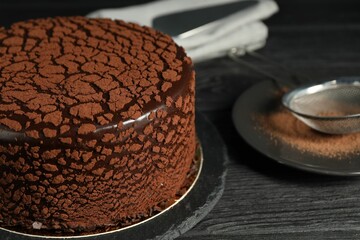 Delicious chocolate truffle cake and cocoa powder on black wooden table, closeup
